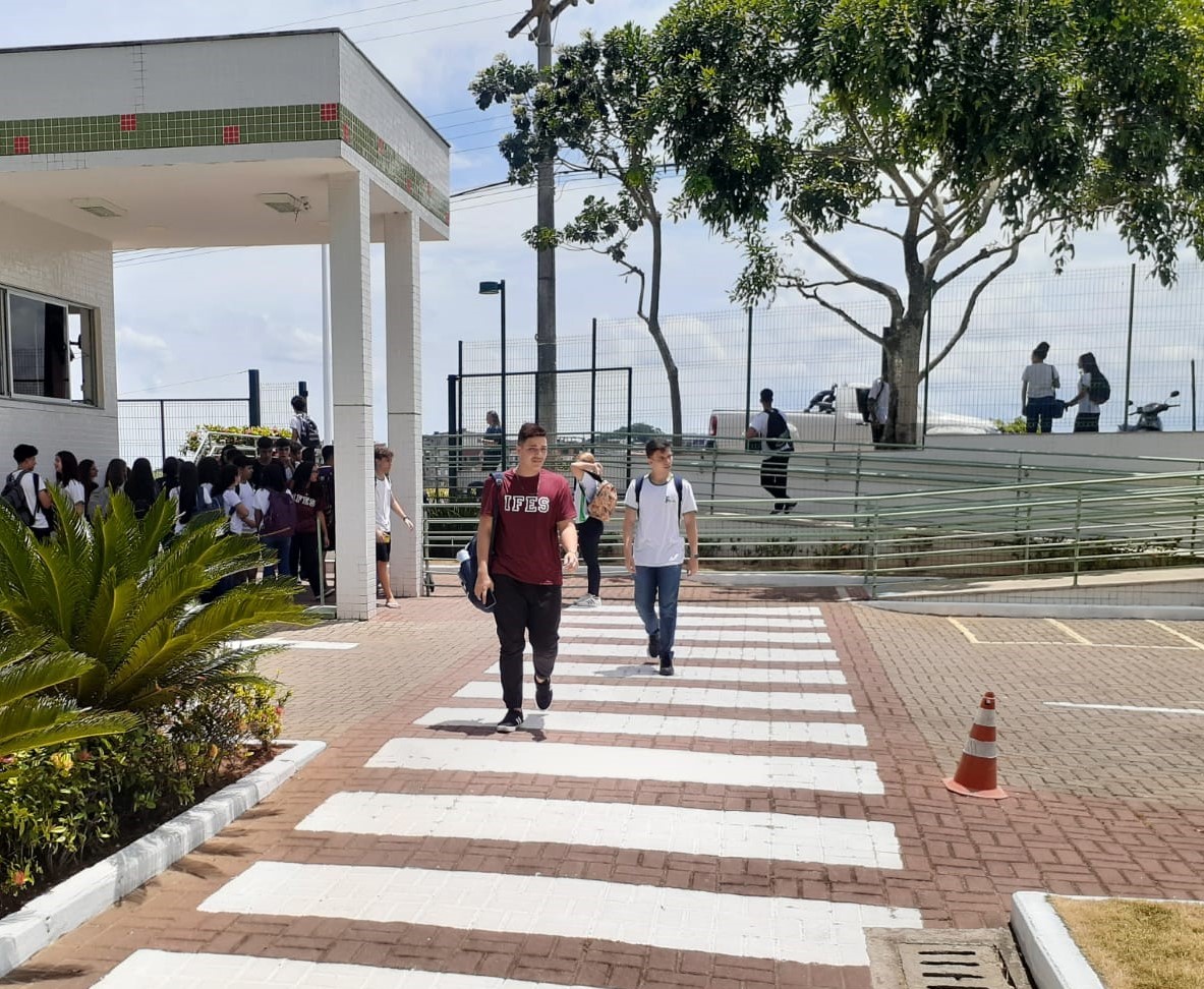 Estudantes se encontram na entrada do campus Guarapari; dois estudantes atravessam a faixa de pedestres que dá acesso ao Bloco A.